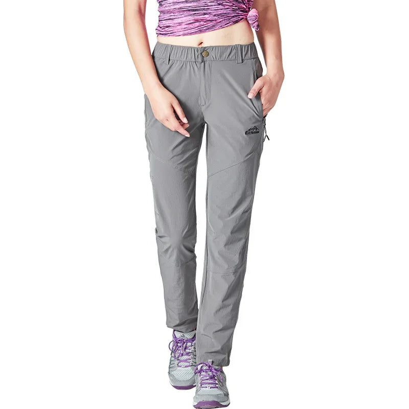 Woman wearing gray outdoor hiking pants with elastic waist and purple sneakers, posing with hands in pockets
