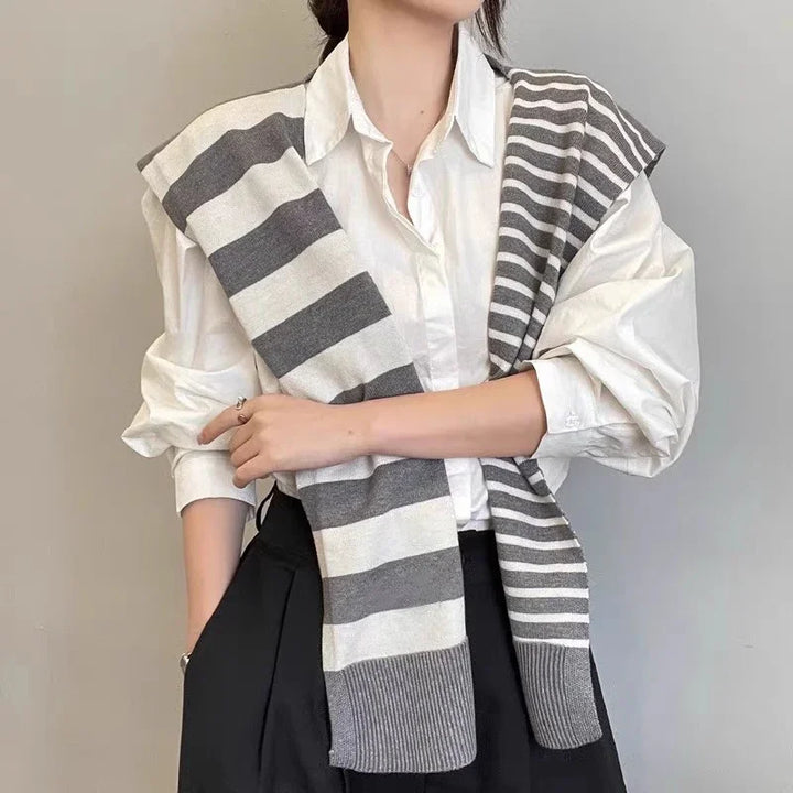 Woman wearing white button-up shirt with gray and white striped sweater draped over shoulders