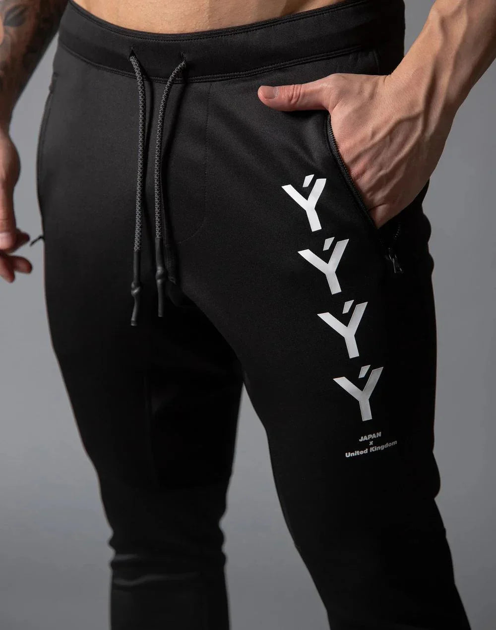 Close-up of black jogger pants with white Y-shaped logos and zippered pocket detail