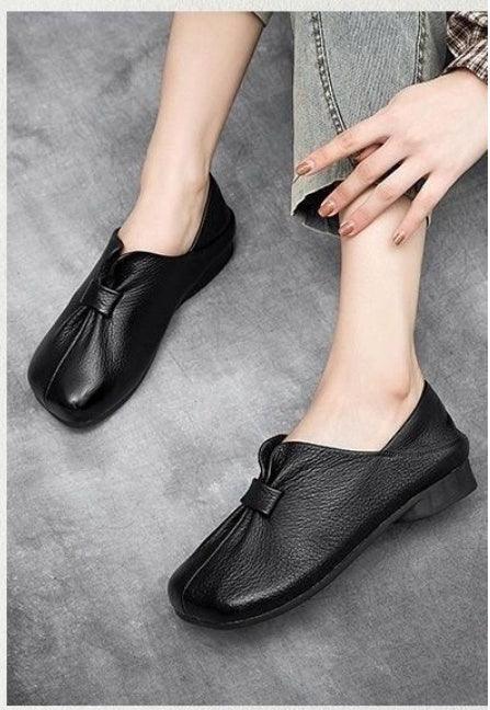 Black leather slip-on flats with a knot detail worn with cropped light-wash jeans on a concrete floor
