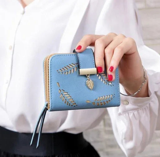 Hand holding a blue leather wallet with cutout leaf designs and a gold leaf charm
