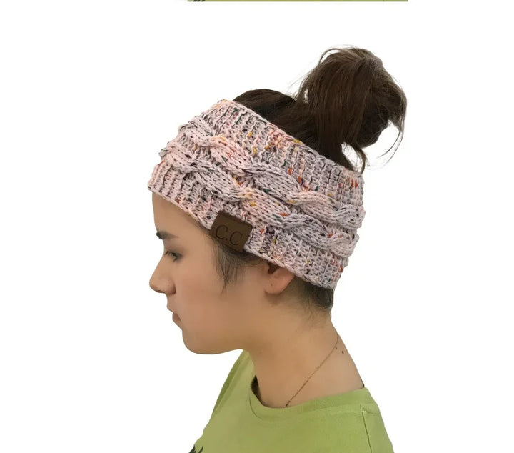 Side view of woman wearing knitted pink cable headband with ponytail hole and CC label