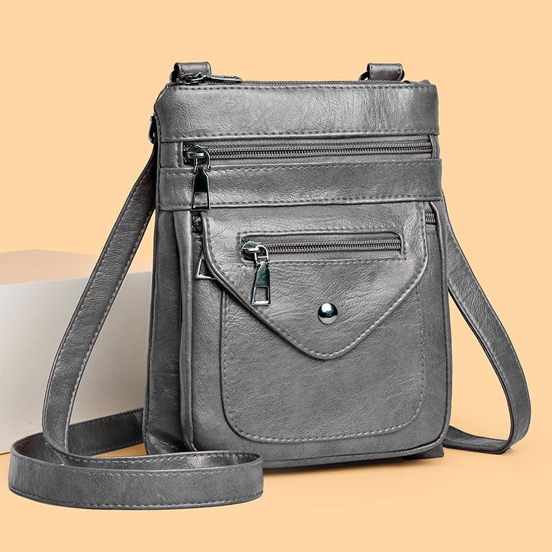 gray leather crossbody bag with front zipper pockets and adjustable strap on beige background