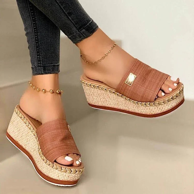 Women's brown wedge sandals with woven platform, gold ankle bracelets, and black skinny jeans