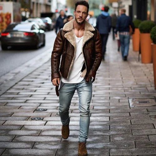 Stylish man walking on city street wearing brown shearling leather jacket, white shirt, light jeans, and brown boots