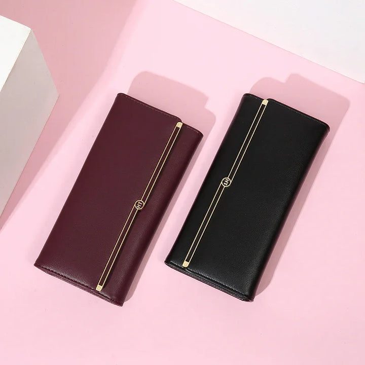 Elegant women's leather wallets in black and burgundy with gold stripe detail on pink background