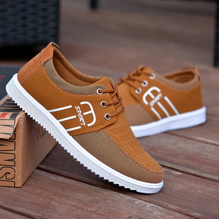 Pair of brown casual sport shoes with white soles and laces on wooden floor with shoebox