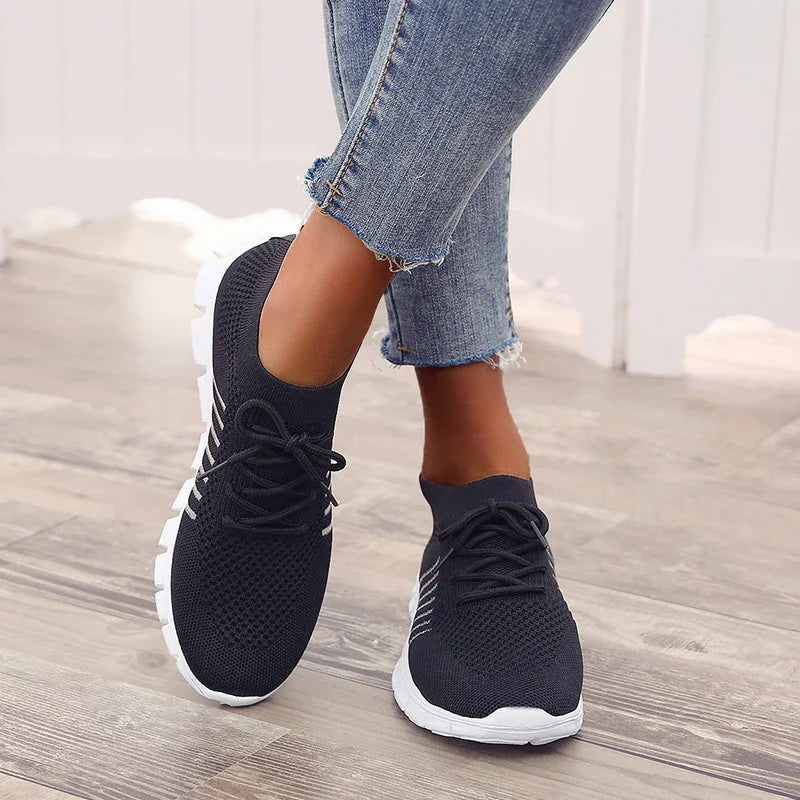 Close-up of feet wearing black knit sneakers with white soles and blue denim jeans on wooden floor