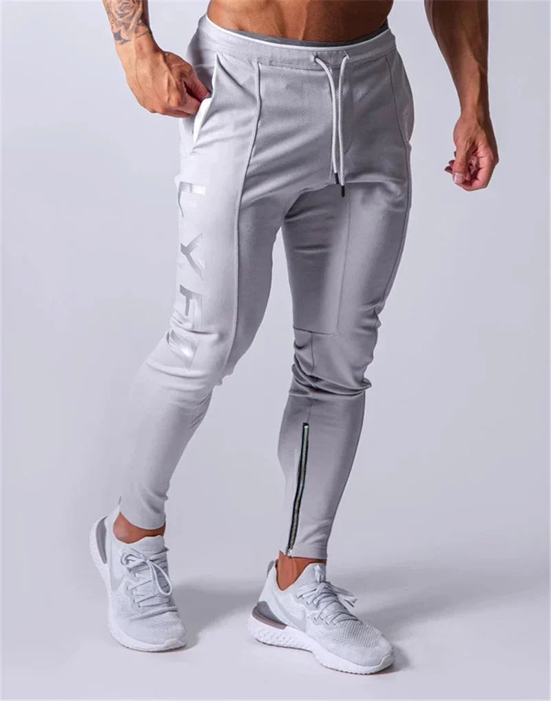 Man wearing light gray slim-fit jogger pants with zipper detail and white sports shoes