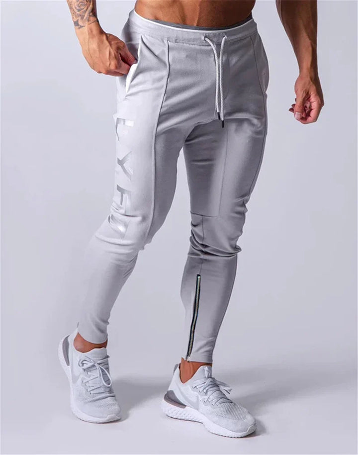 Man wearing light gray slim-fit jogger pants with zipper detail and white sports shoes