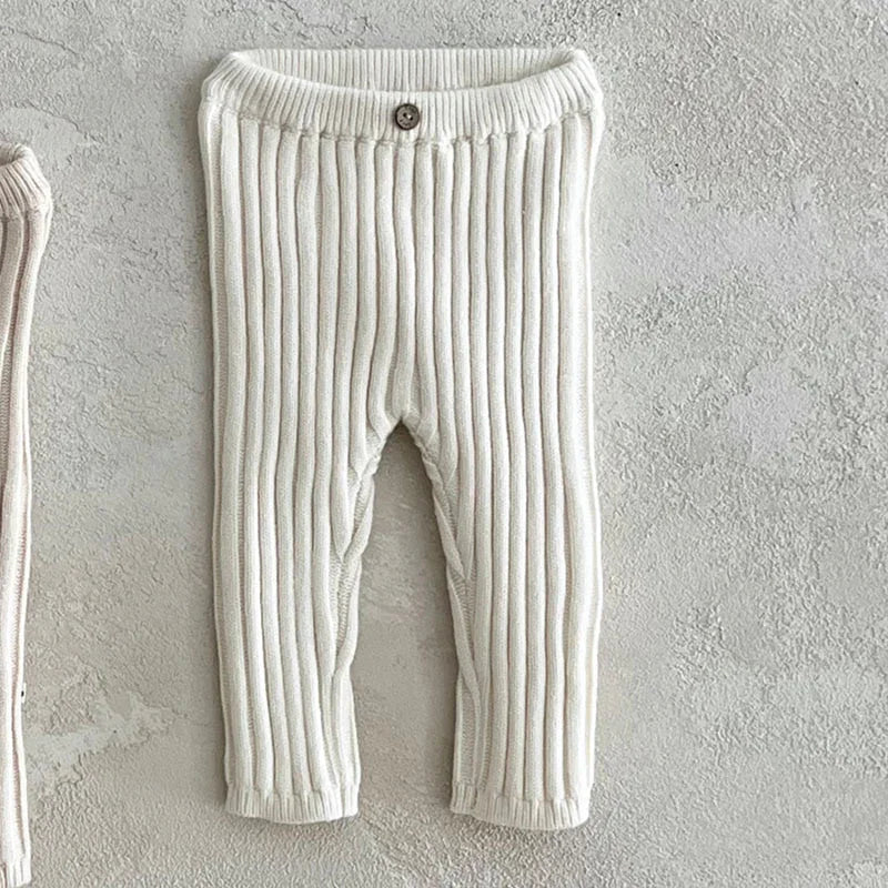 Cream ribbed knit baby pants with button detail on waist, displayed on textured gray background