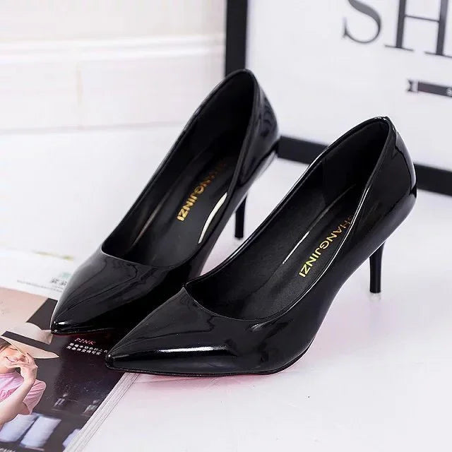 Pair of black patent leather stiletto heels with pointed toes on white surface