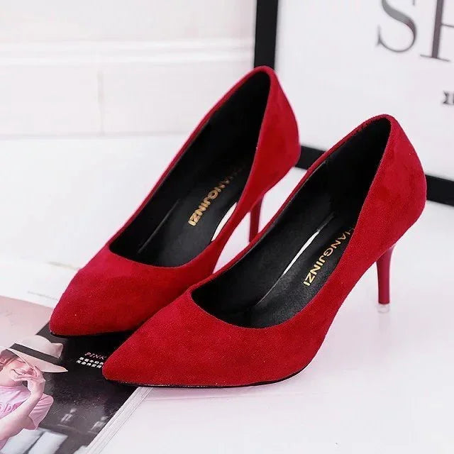Pair of elegant red suede high heel shoes with pointed toes on white surface