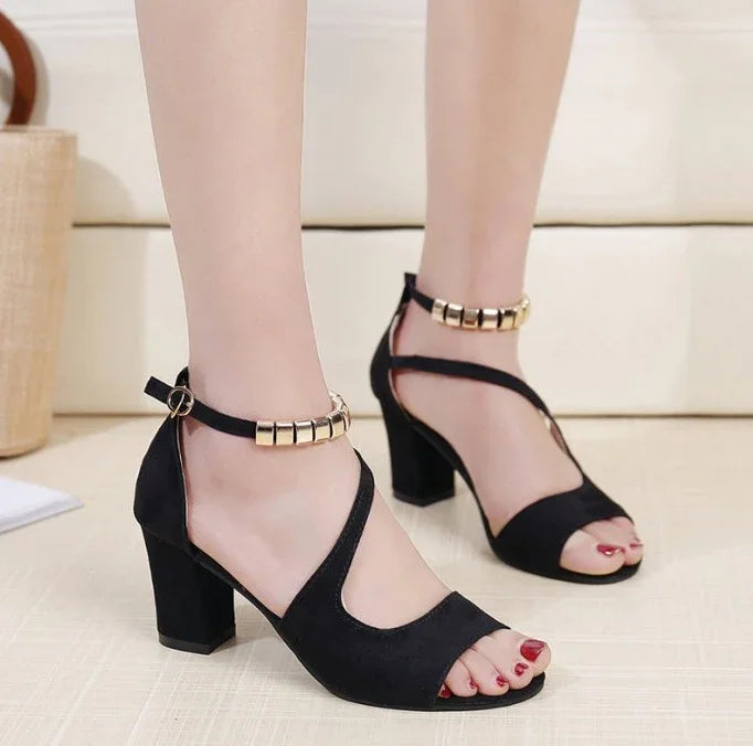 Black suede block heel sandals with gold accents and ankle straps worn on feet with red nail polish