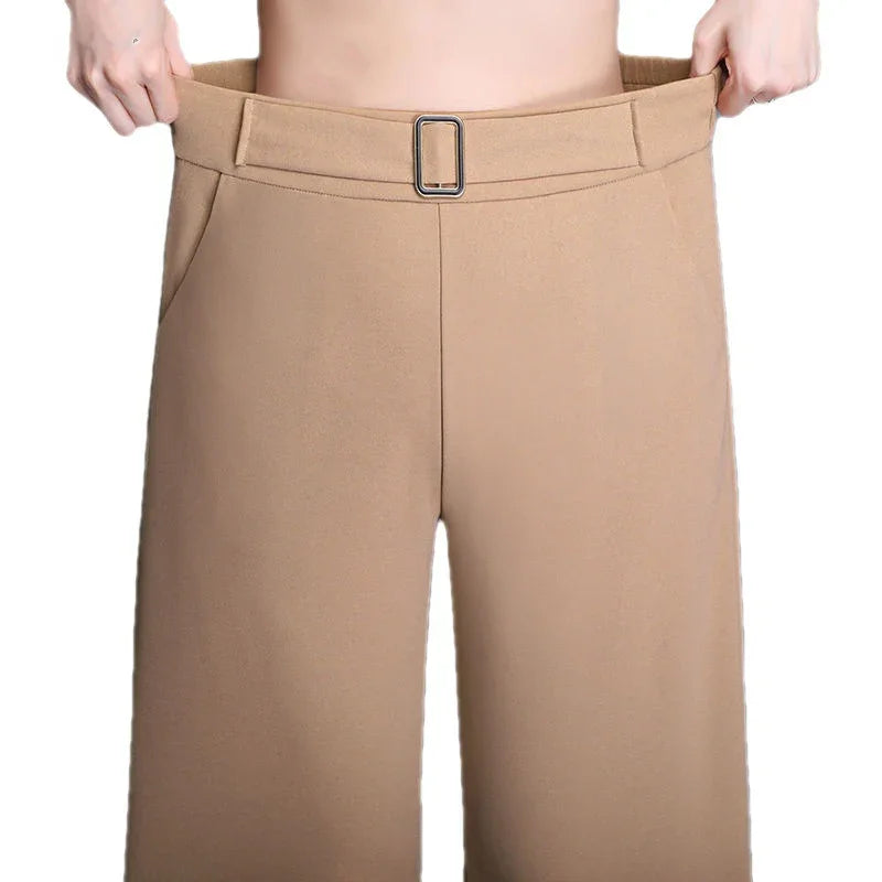 Person holding out waistband of loose beige wide-leg pants with belt detail