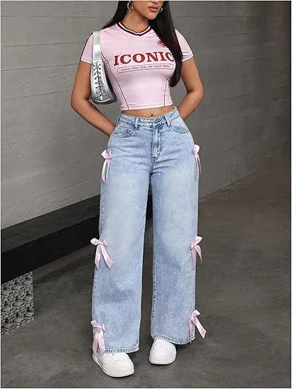 Woman wearing pink crop top with ICONIC print, light blue high-waisted jeans with pink bows, white sneakers
