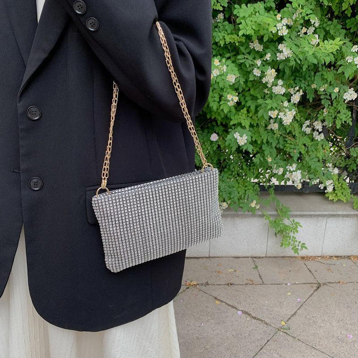 Woman in black blazer carrying a silver rhinestone clutch bag with gold chain strap outdoors