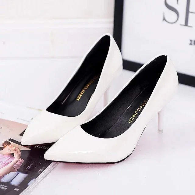Pair of elegant white patent leather high heels with pointed toes on a white surface