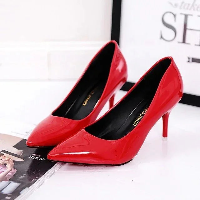 Pair of shiny red patent leather high heel shoes on white surface near magazine