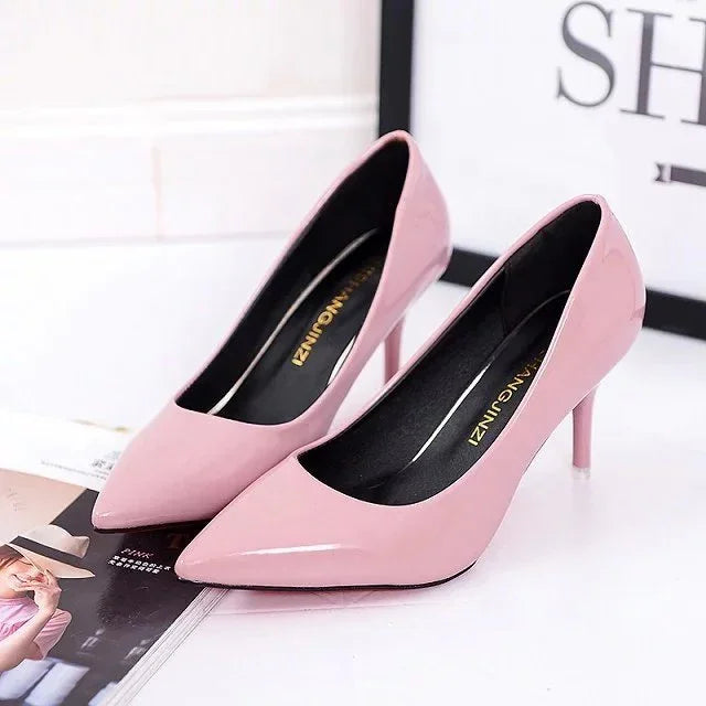 Pair of pink patent leather high heel shoes with pointed toes on a white surface
