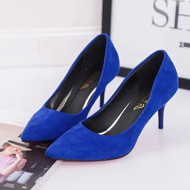 Pair of royal blue suede high heel pumps with pointed toes on a white surface