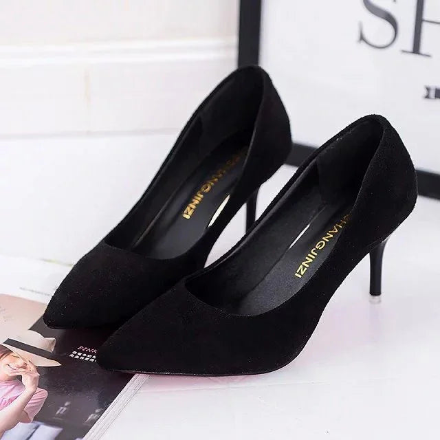 Pair of elegant black suede high heel pumps on a white surface with magazine background