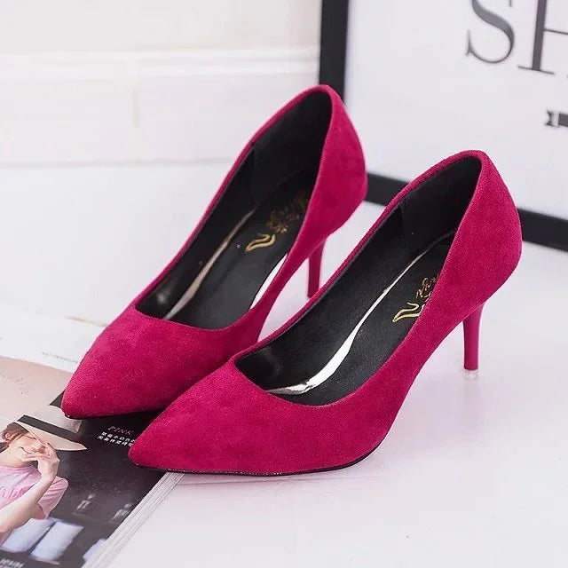 Pair of elegant magenta suede high heel shoes with pointed toes on a white surface