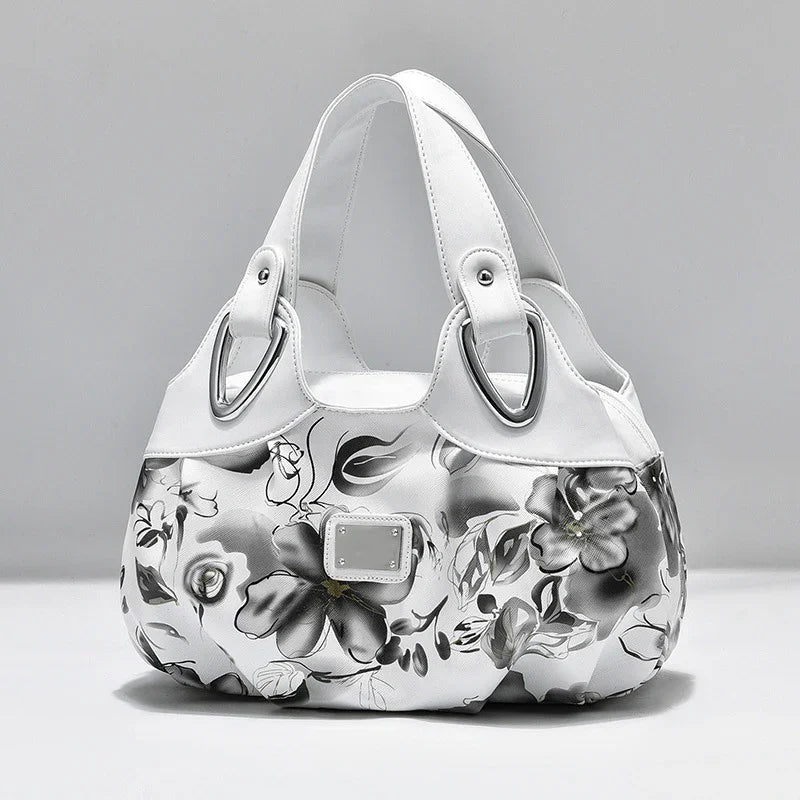 white handbag with black floral print and silver-tone hardware on grey background