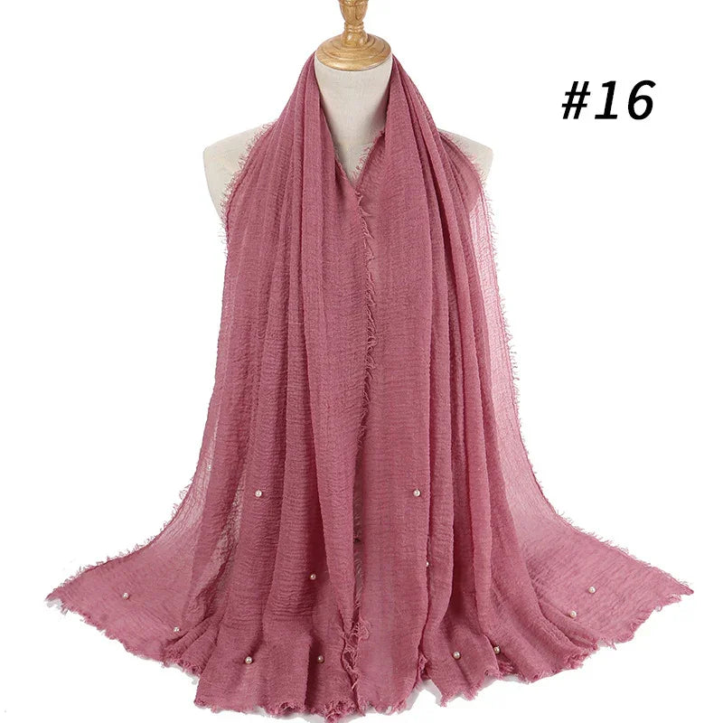 Soft pink textured scarf with frayed edges and small pearl embellishments displayed on a mannequin