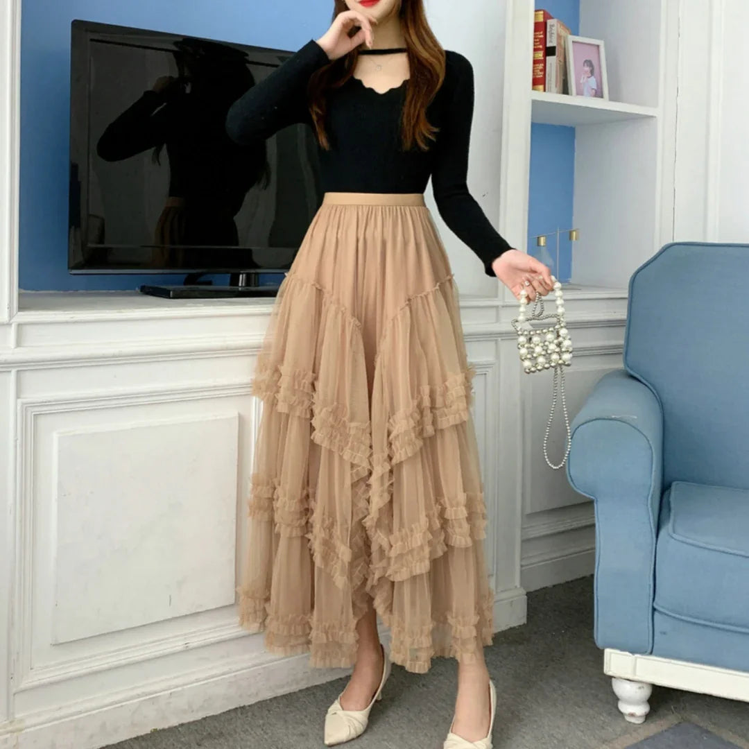 Woman wearing beige layered tulle skirt and black long sleeve top holding pearl handbag indoors
