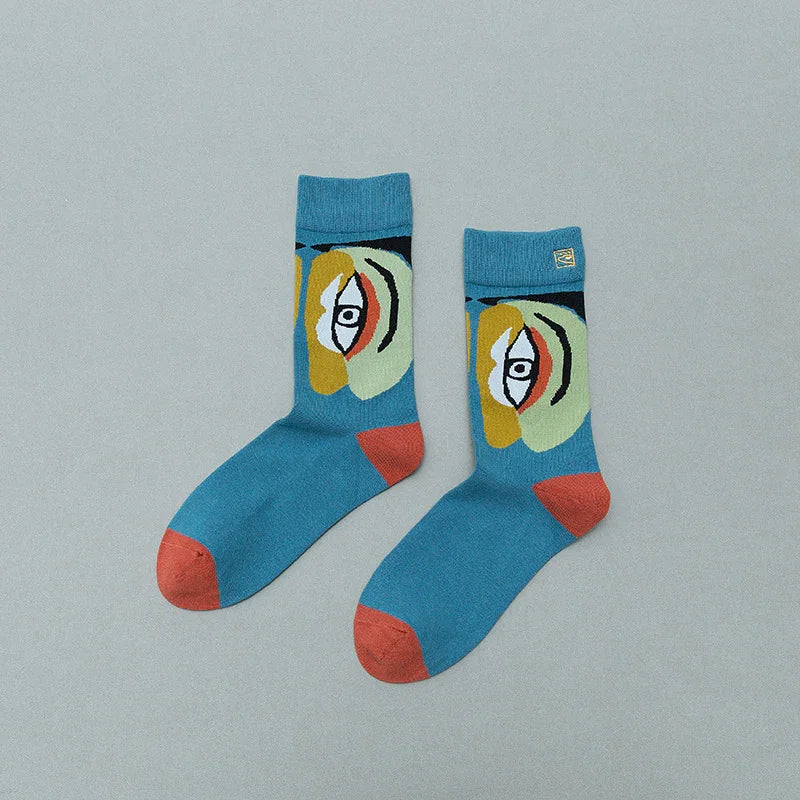 Blue crew socks with abstract face design and orange toes and heels on light gray background
