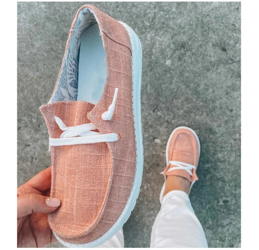 Close-up of pink textured casual slip-on shoe with white laces and sole, worn with white pants on concrete