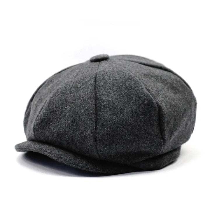 Dark gray wool newsboy cap with paneled design and button on top, isolated on white background