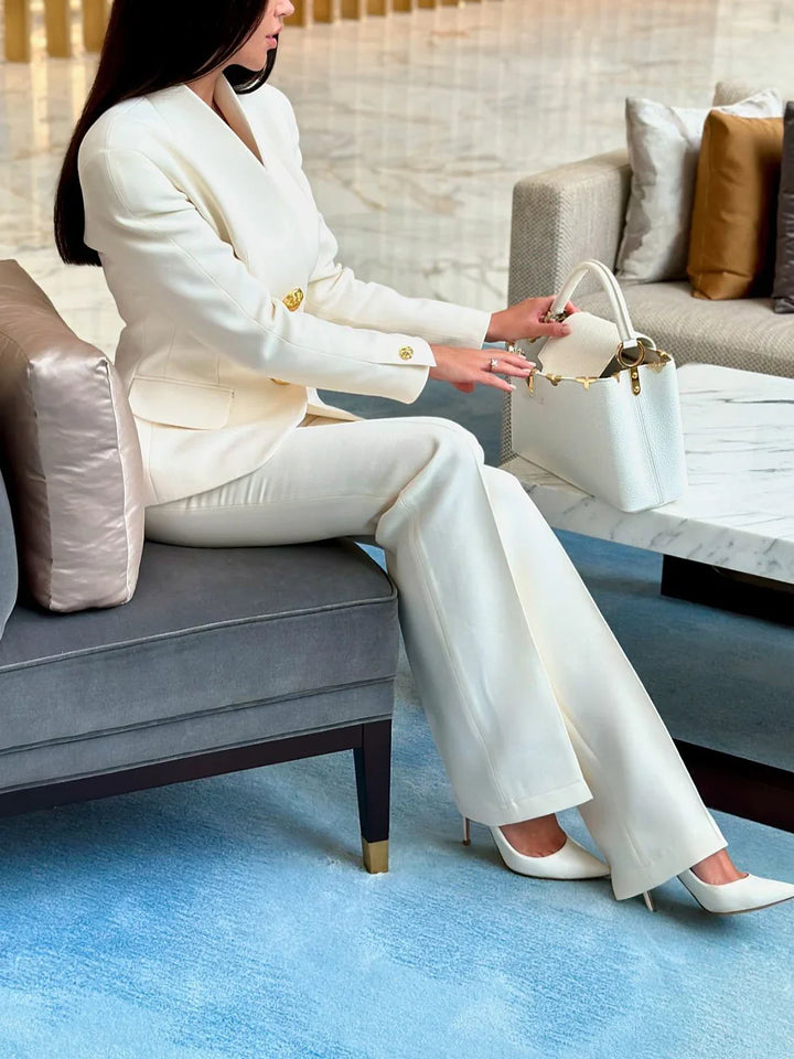 Woman in white suit sitting on gray sofa holding a white designer handbag in chic modern lounge