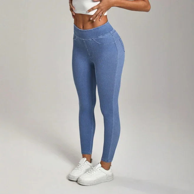 Slim woman modeling high-waisted blue leggings and white sneakers on plain background