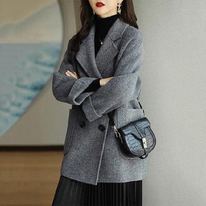 Woman wearing grey double-breasted coat with black turtleneck and black croc-embossed handbag indoors