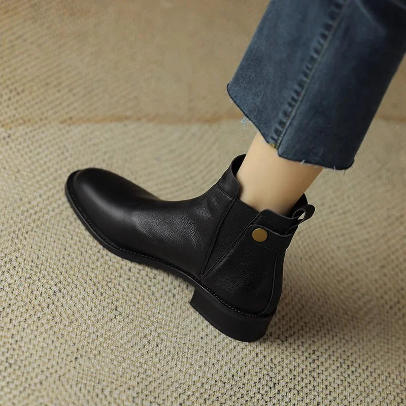 Black leather ankle boot with low heel worn with cropped blue jeans on textured beige carpet