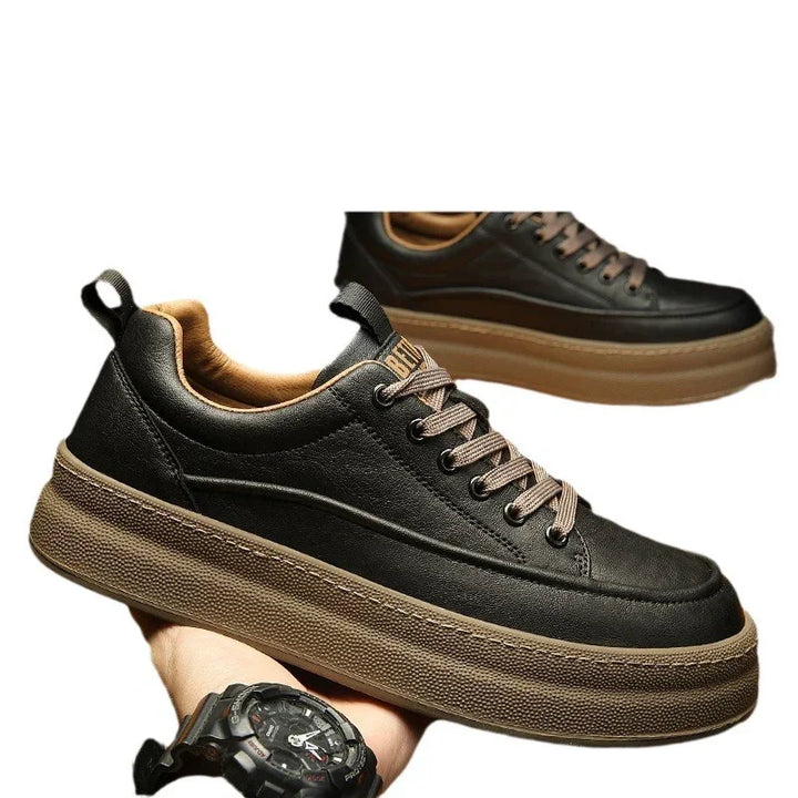 Black leather sneakers with thick brown rubber soles and tan inner lining held in hand
