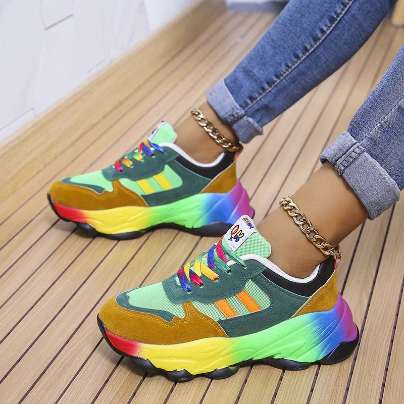 Colorful rainbow chunky sneakers with green, orange, and brown panels worn with rolled-up jeans and gold chain anklets on wooden floor