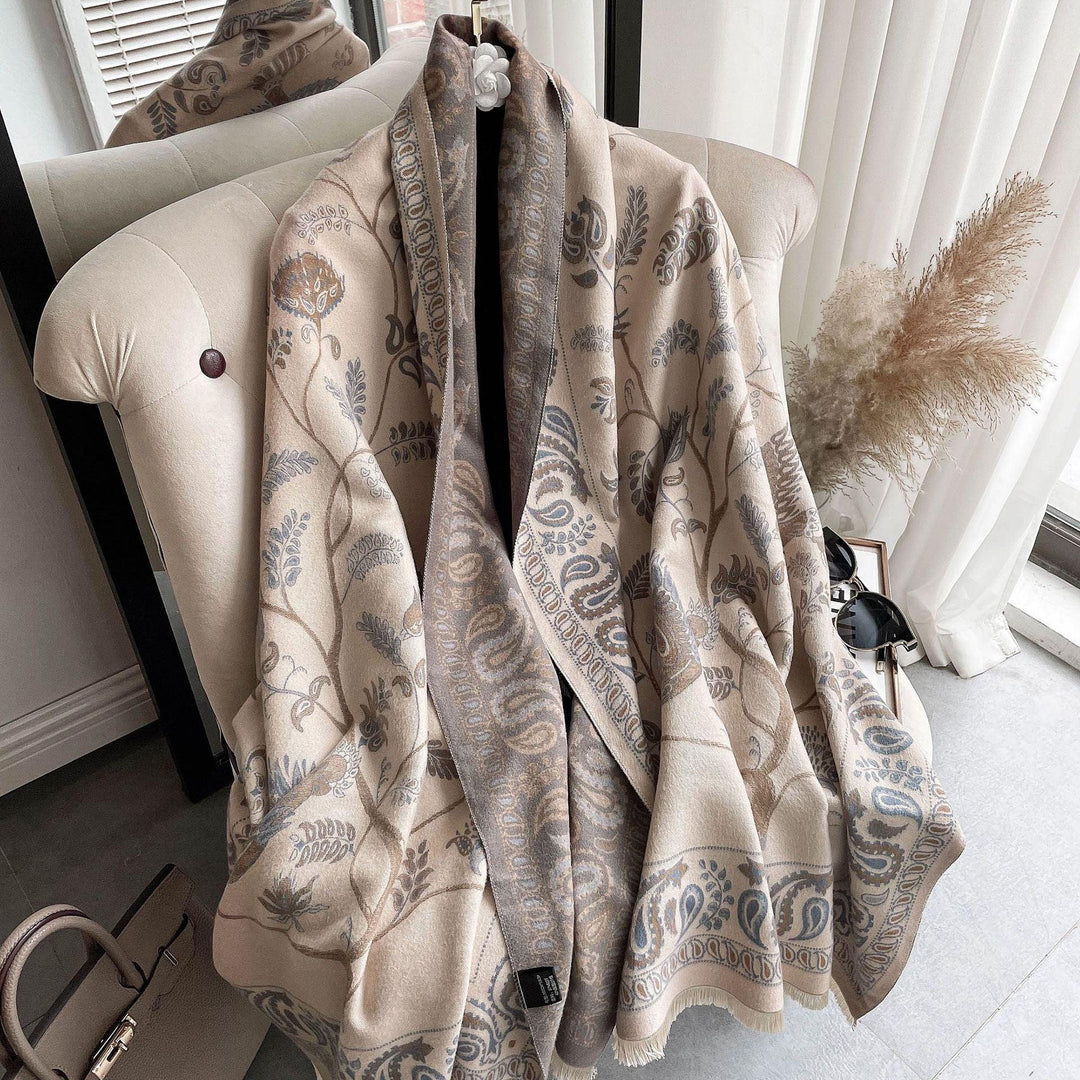 Beige and gray floral patterned shawl draped over a cream tufted armchair near window with pampas grass and sunglasses