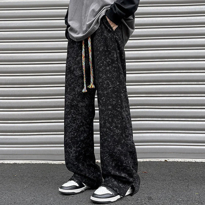 Person wearing black patterned wide-leg pants with multicolored drawstring and black white sneakers