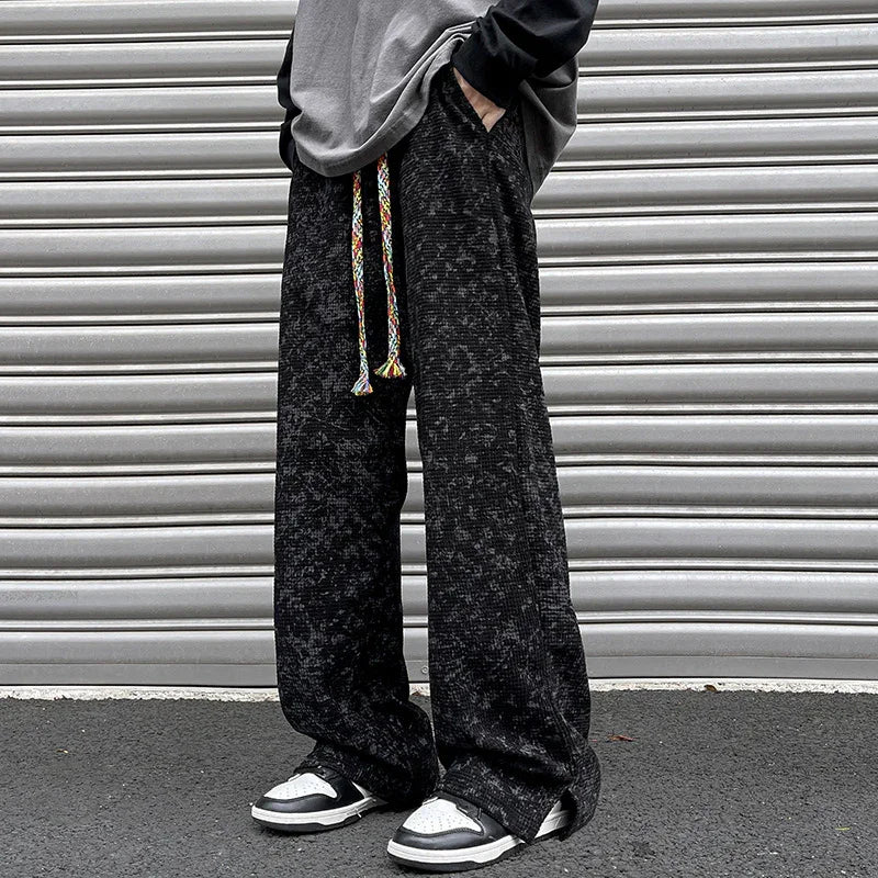 Person wearing loose black textured pants with colorful drawstring and black white sneakers against metal shutter