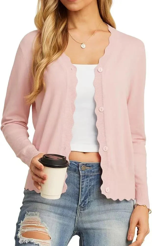 Woman wearing light pink scalloped edge cardigan, white crop top, ripped blue jeans, holding coffee cup