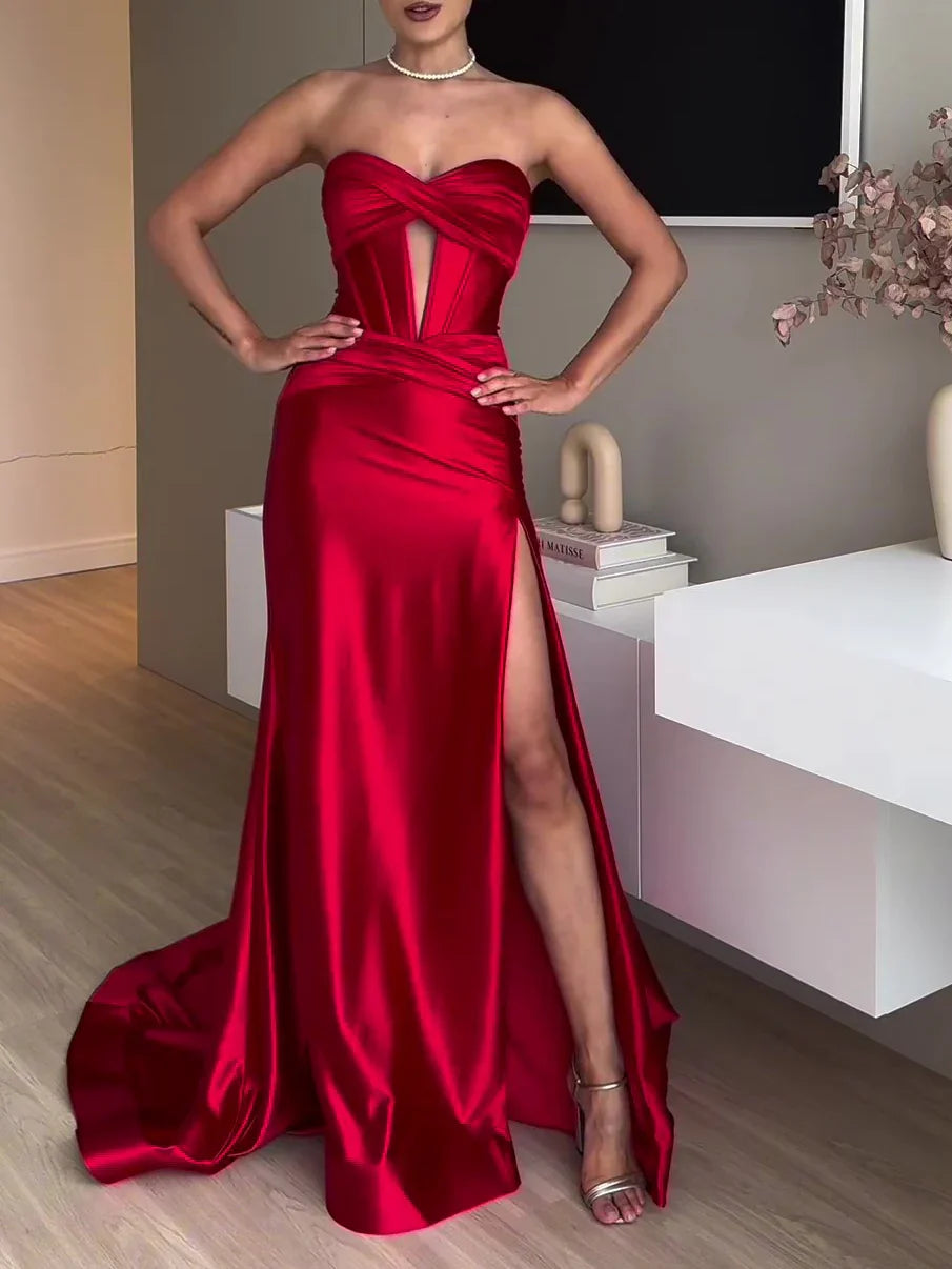 Woman in elegant red satin strapless evening gown with thigh-high slit and pearl necklace in modern interior