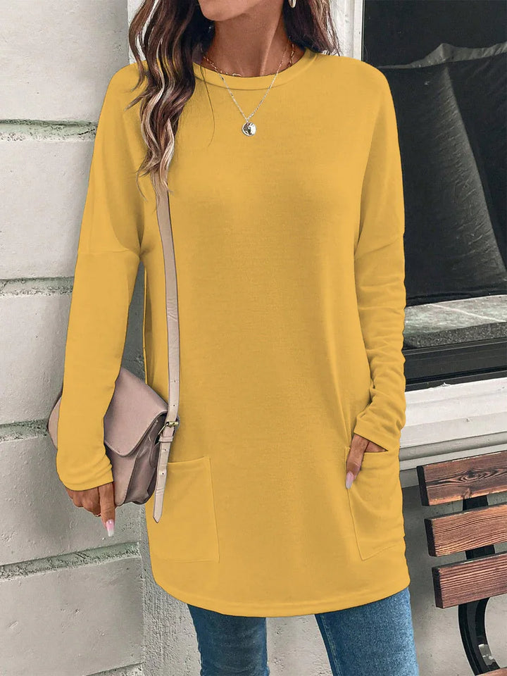 Woman wearing mustard yellow long sleeve tunic sweater with front pockets and crossbody bag indoors
