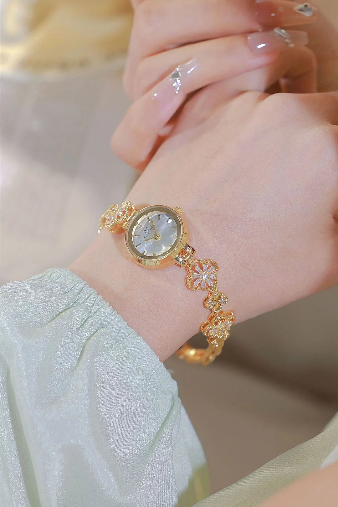 Elegant gold floral bracelet watch with mother-of-pearl dial on a wrist, paired with manicured nails