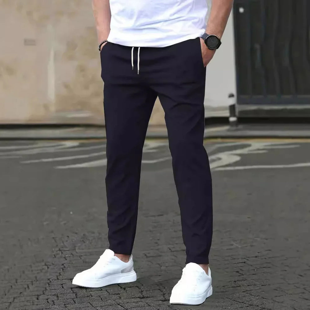 Man wearing black jogger pants with white drawstrings and white sneakers standing on paved street