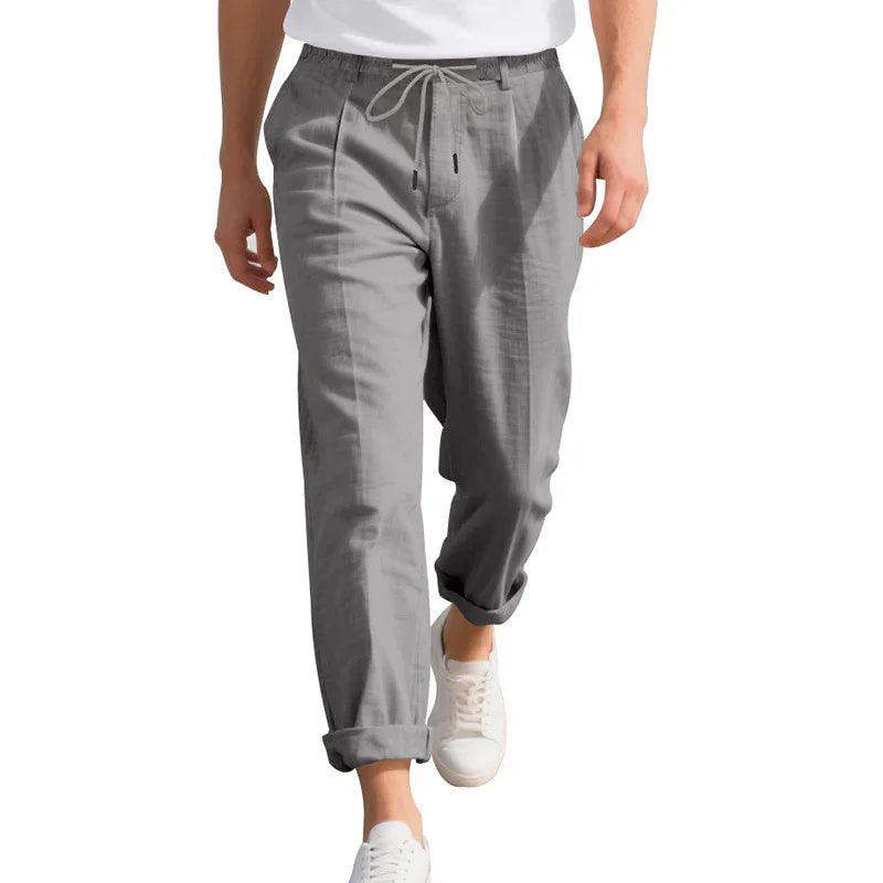 Man wearing gray drawstring pants with rolled cuffs and white sneakers on white background
