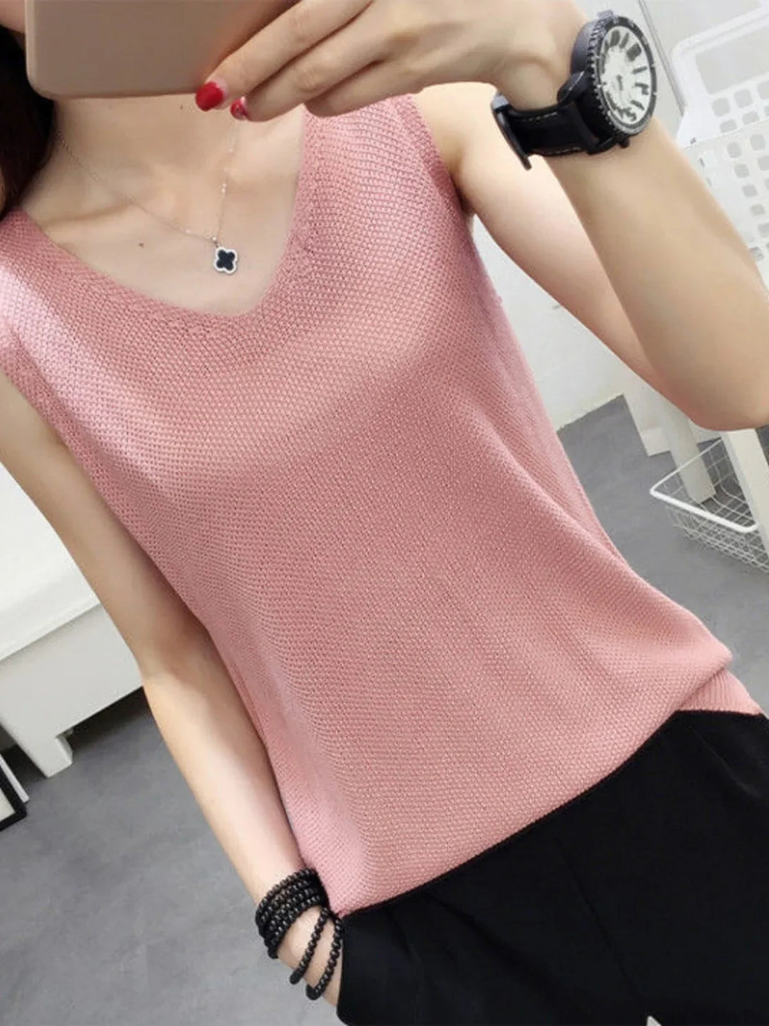 Woman wearing a pink knit sleeveless top, black pants, black beaded bracelet, and black watch