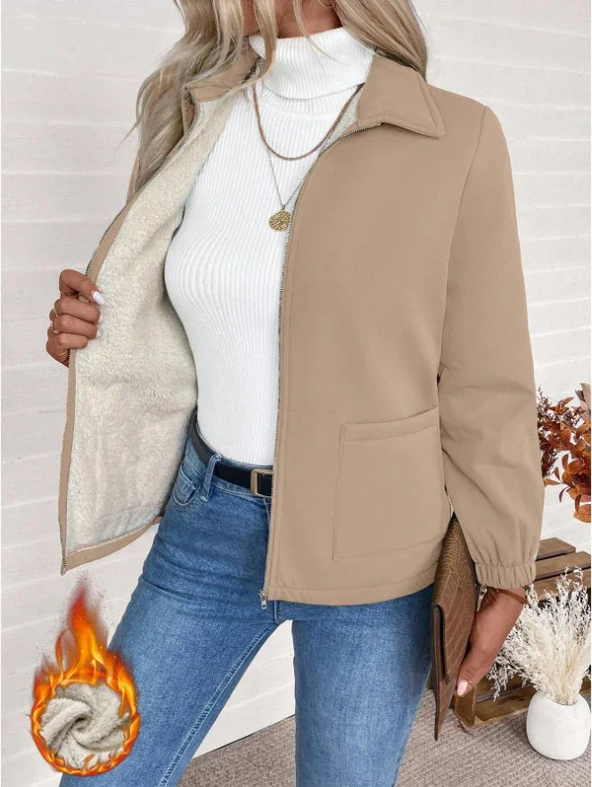 Woman wearing beige fleece-lined jacket over white turtleneck sweater with blue jeans and accessories